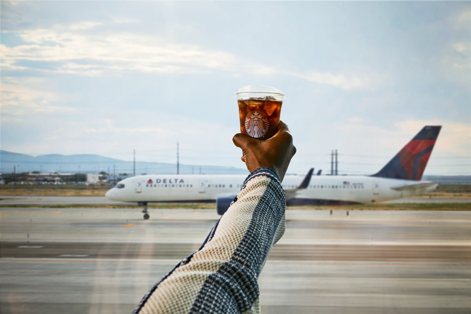 A person holding a Starbucks iced coffee in front of a Delta plane