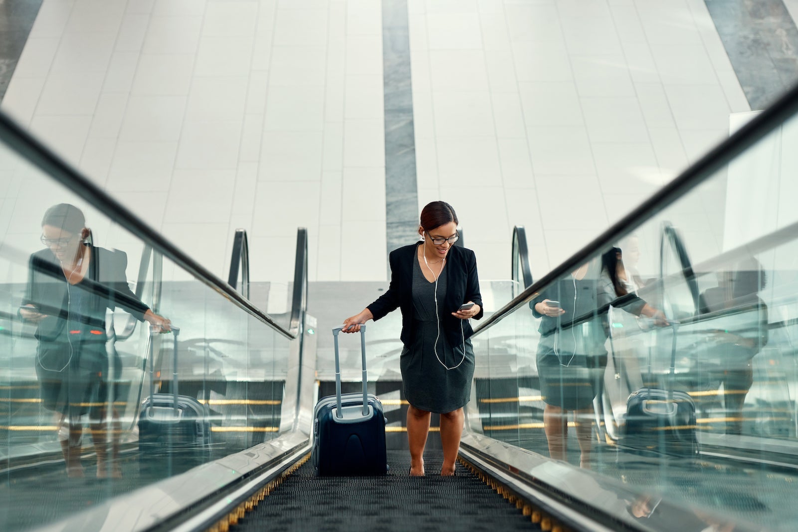 Shot of a young businesswoman using a mobile phone while traveling on an escalator in an airport