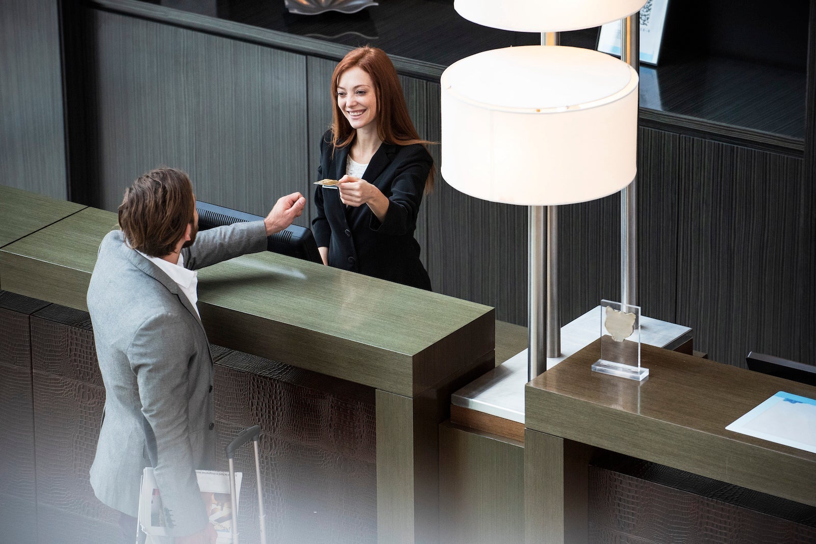 Smiling female receptionist giving credit card to businessman while standing at hotel reception.