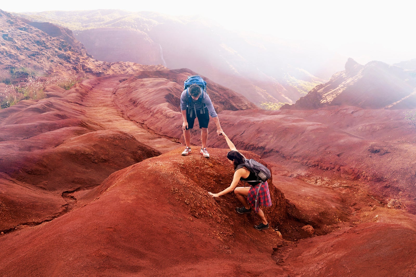 A man and a woman hiking on red rocks in Hawaii