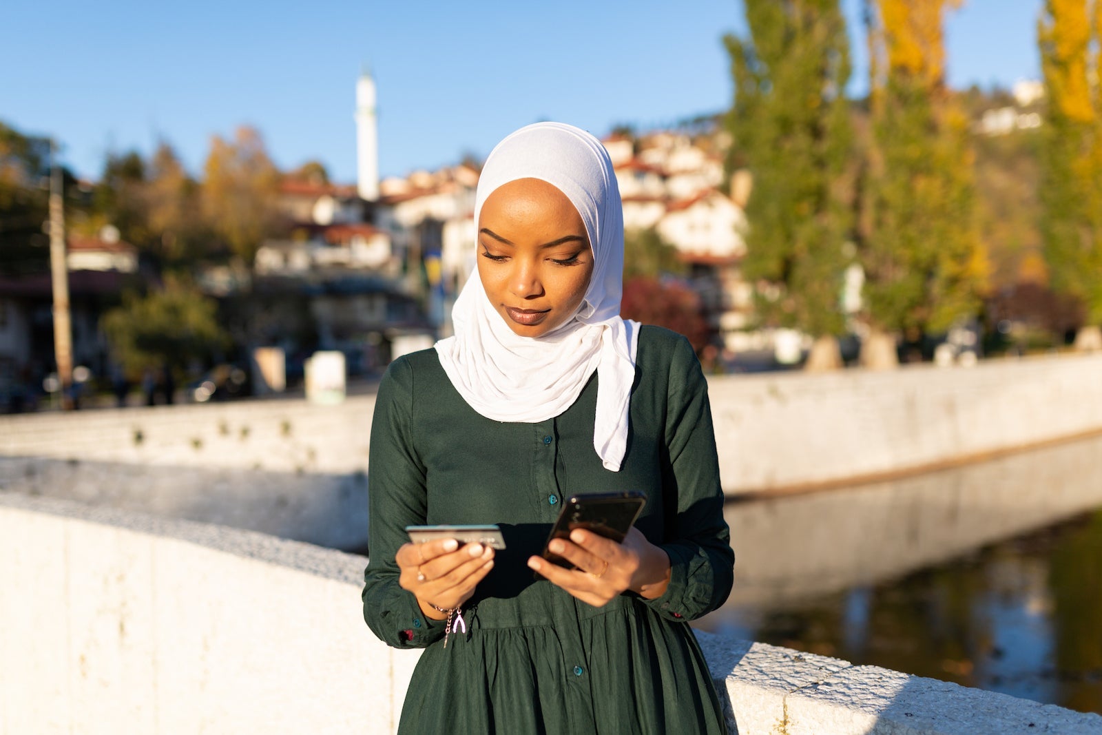 a woman wearing hijab makes a phone call while holding a credit card