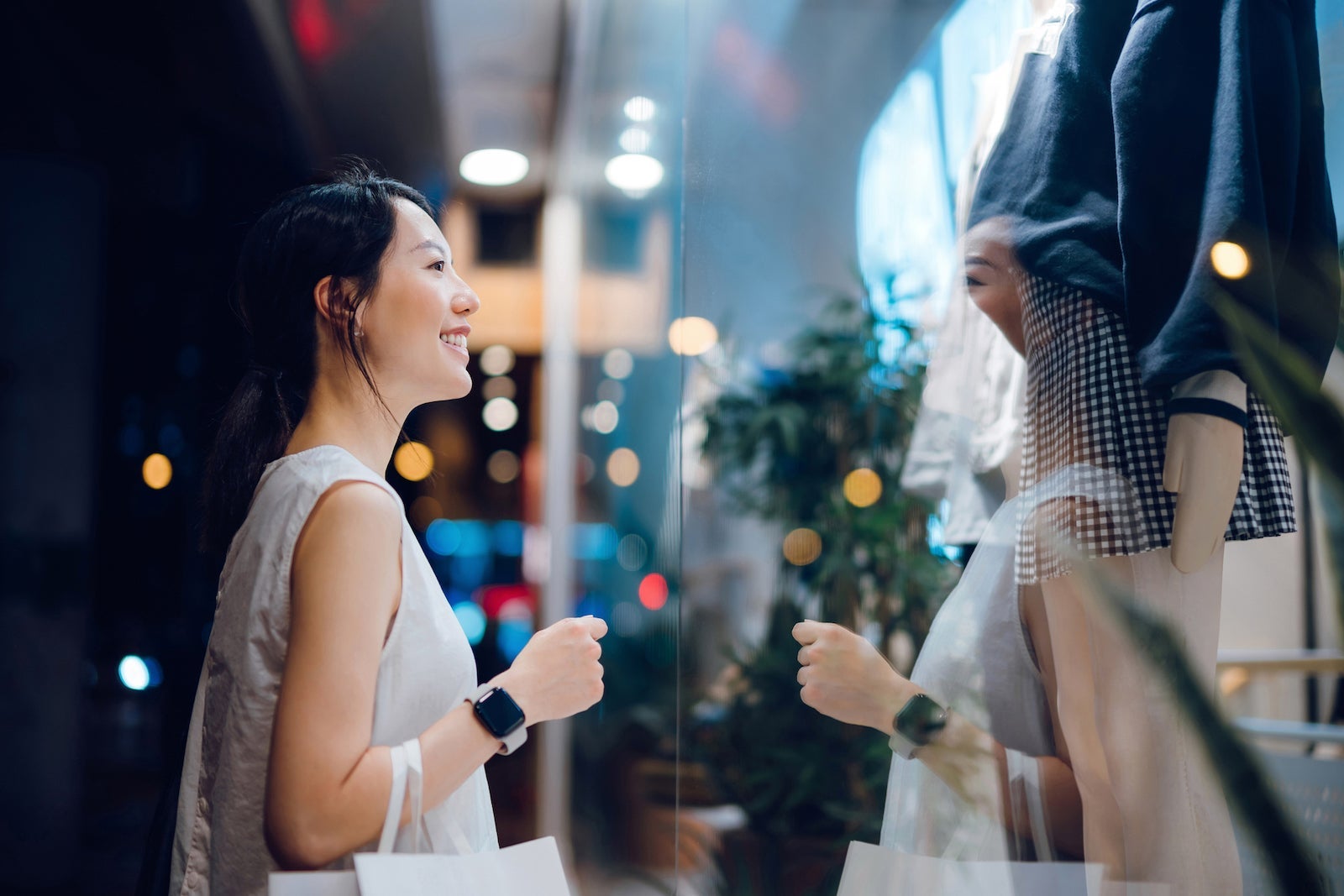a smiling Asian woman looks through a glass window at store displays