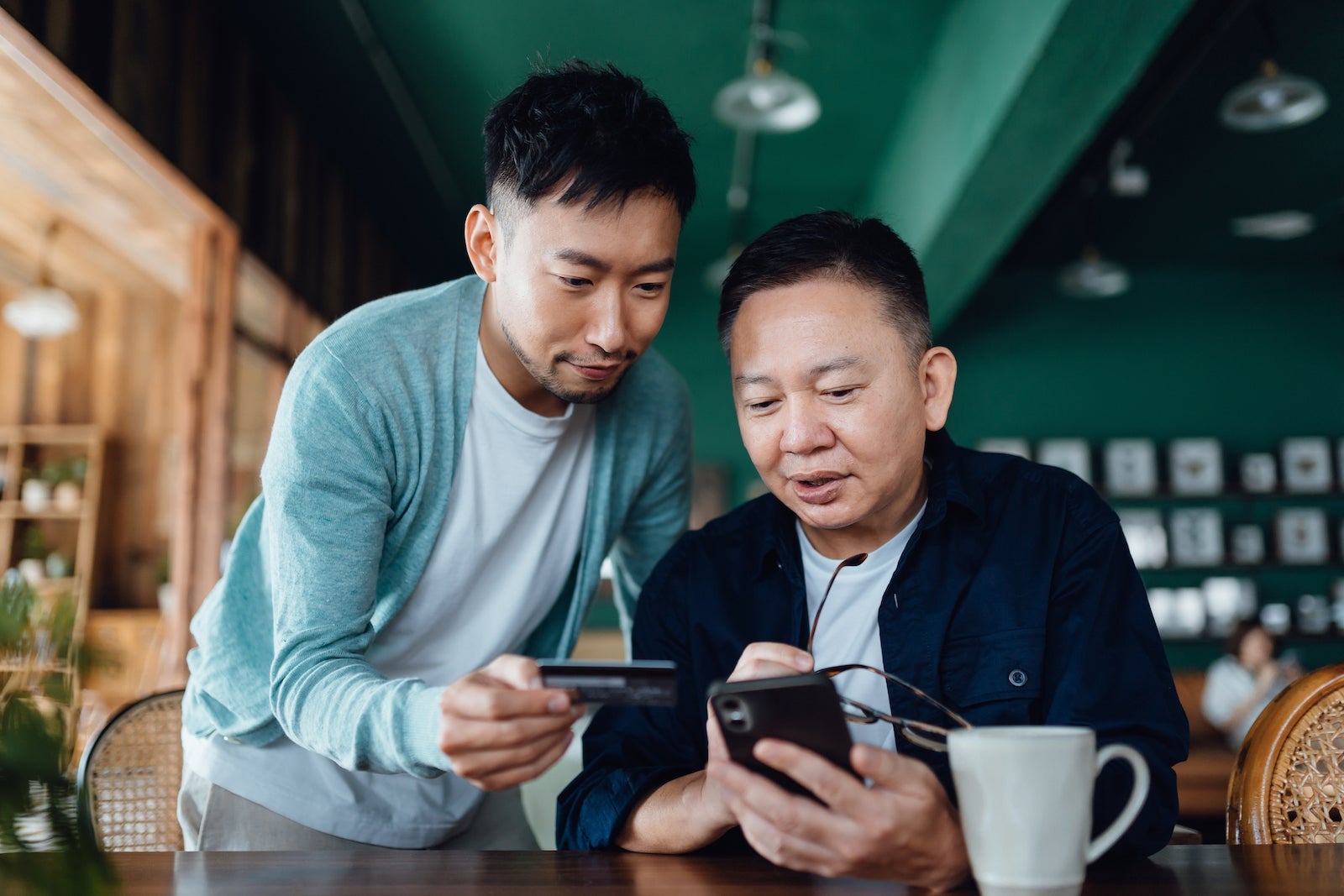 an Asian father and son use a credit card to shop online together