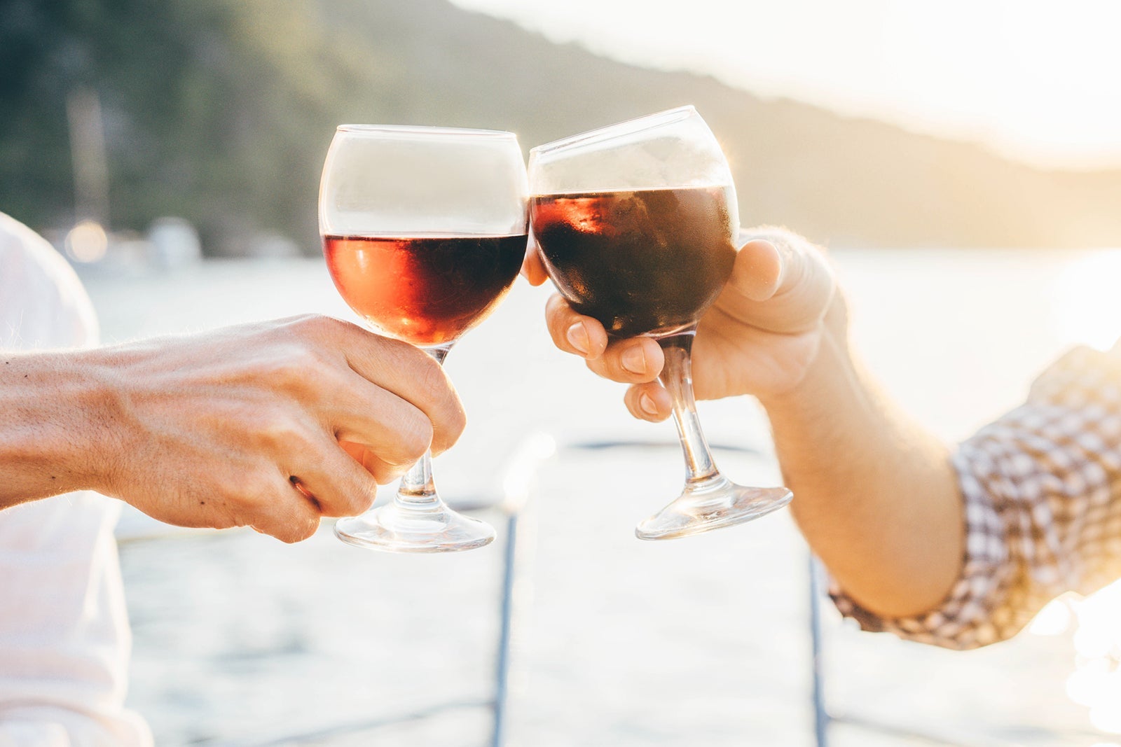 A close-up of two hands, each holding a glass of wine and toasting