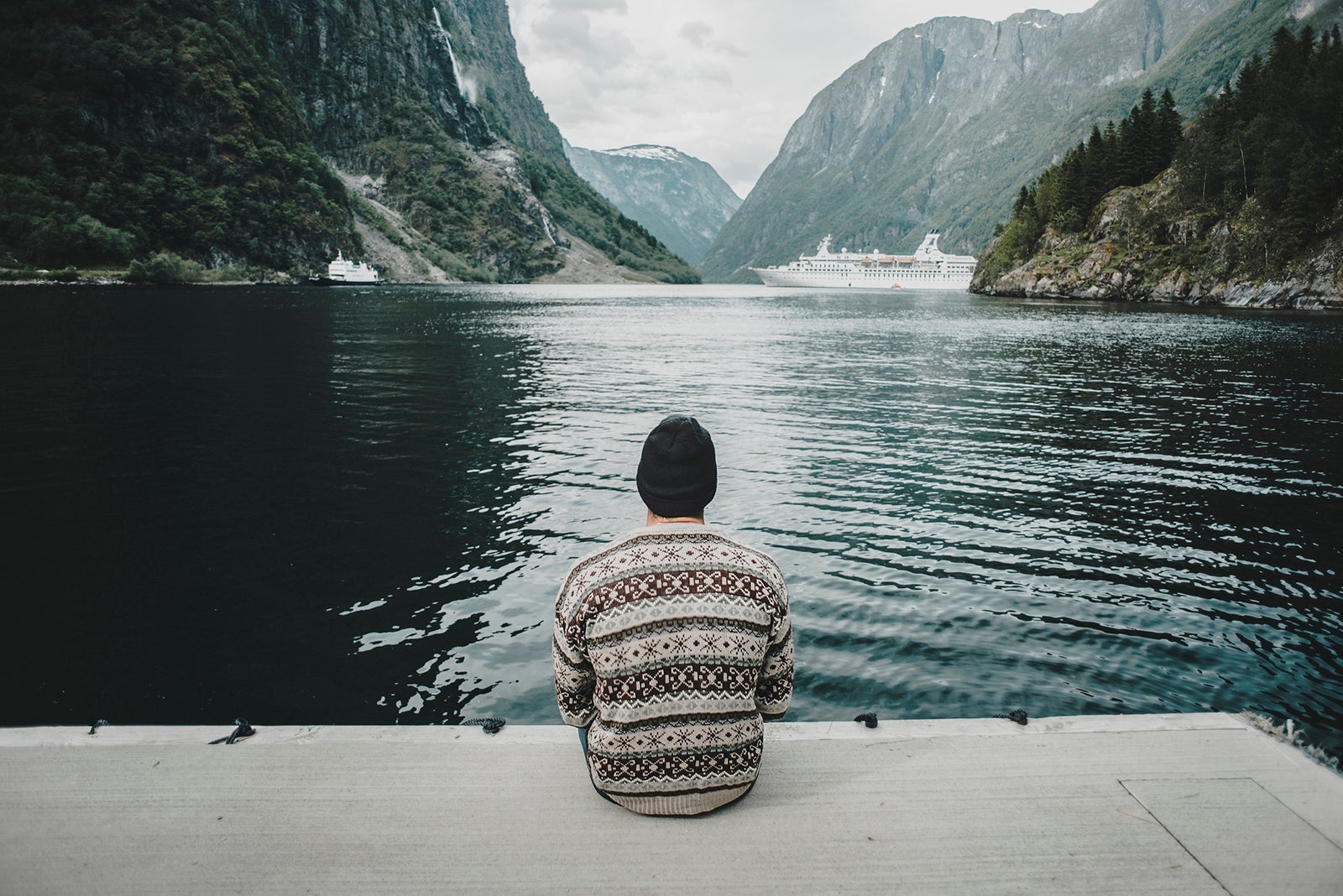 man sitting on dock watching cruise ship