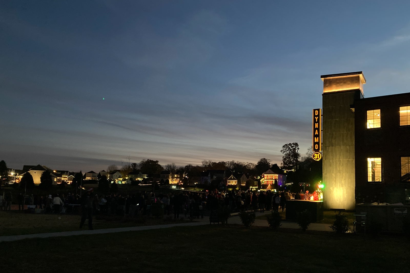 visitors in a parking lot wait for Christmas lights to turn on as the sun sets
