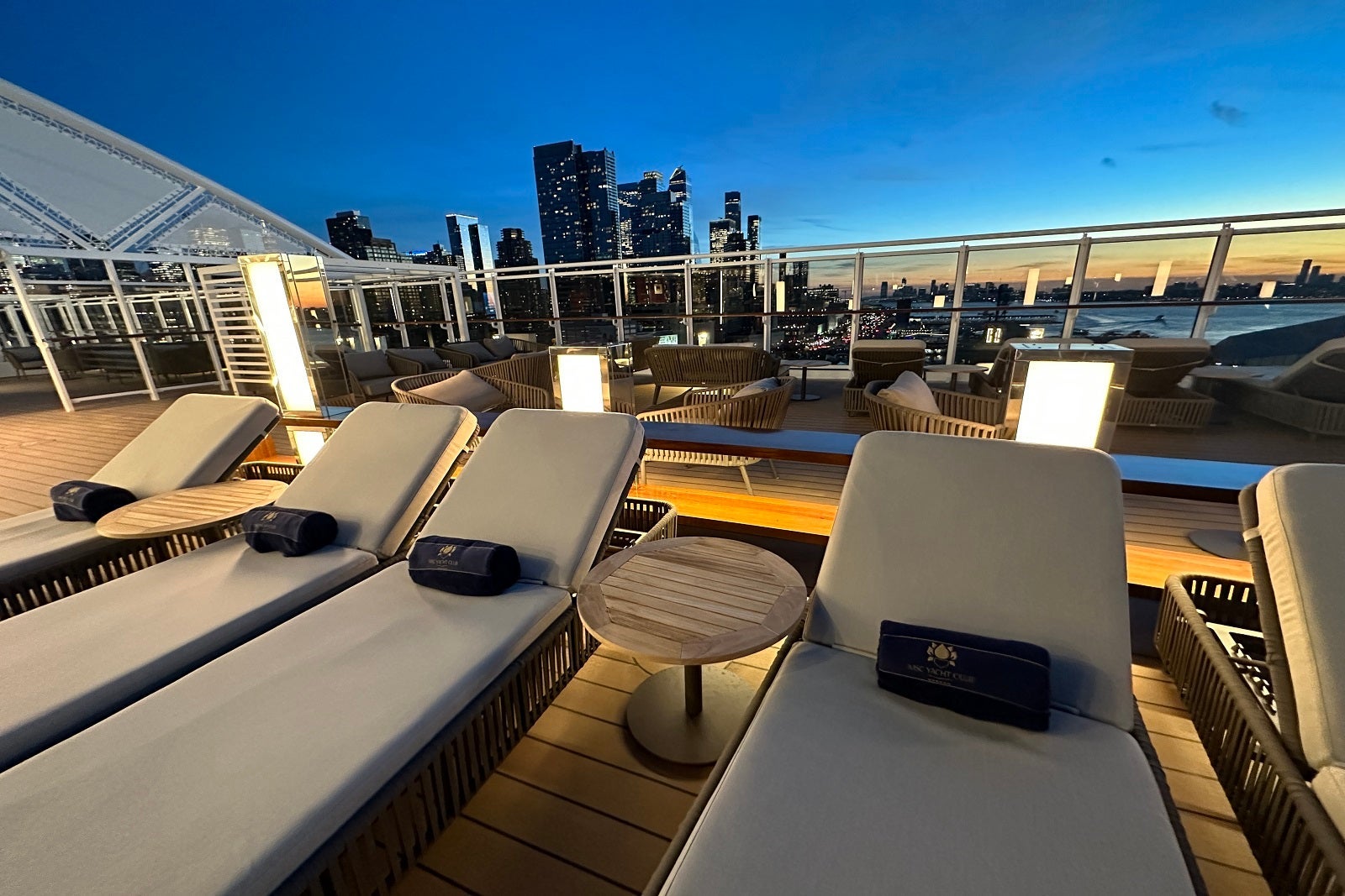 The dedicated Yacht Club pool deck area on MSC Cruises' MSC Seascape with lounge chairs against an evening cityscape