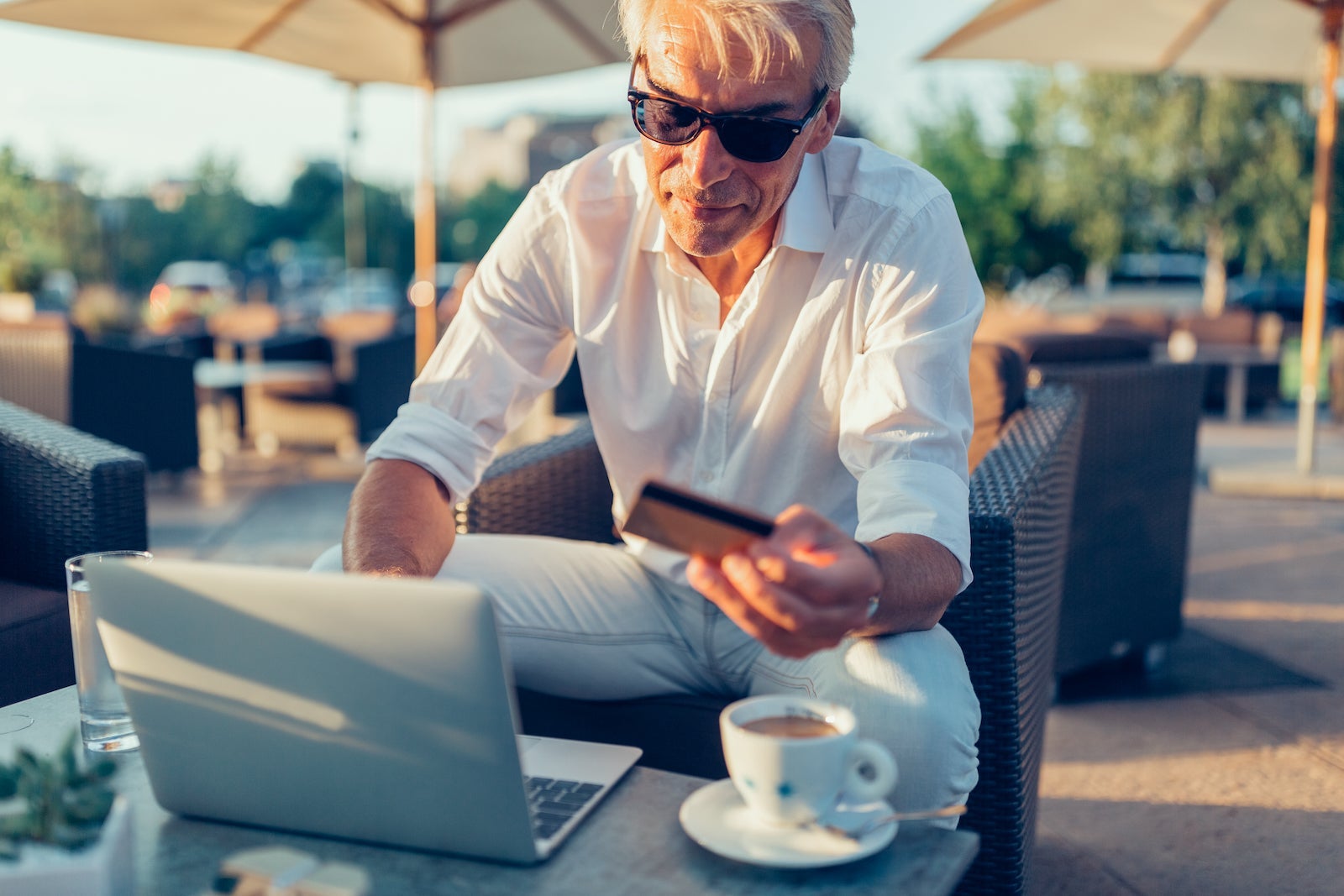 a man sits outside a luxury resort using his laptop to shop online