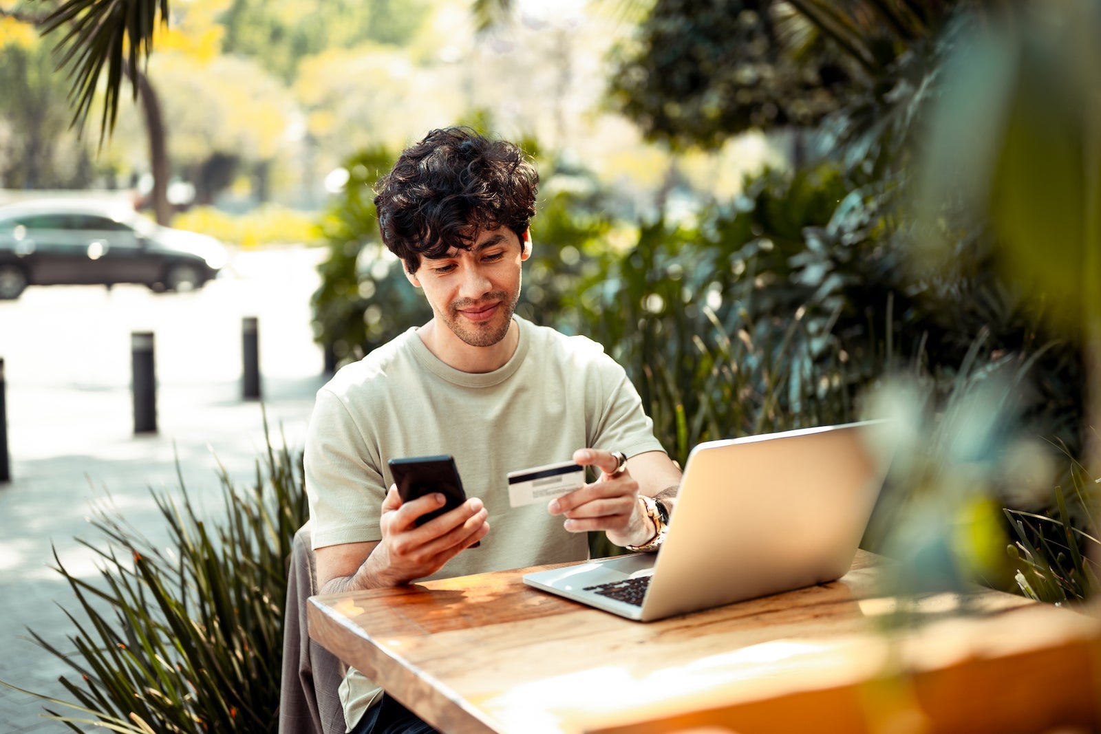 A young person sits at a computer while holding a phone and a credit card