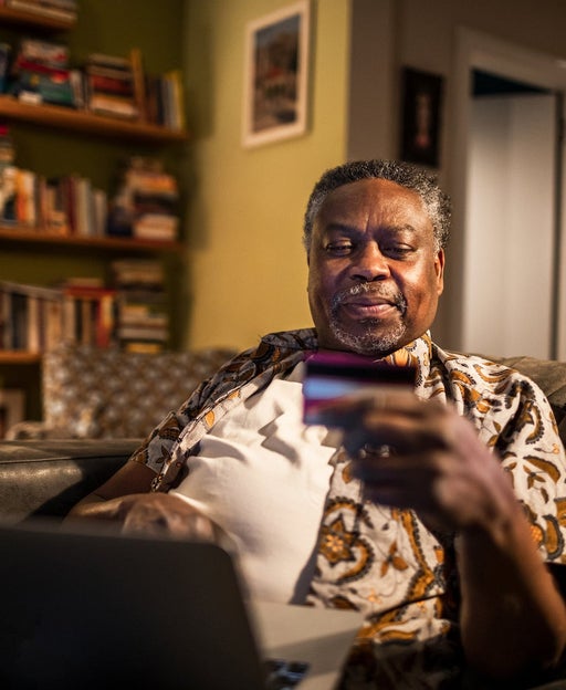 a senior citizen holds a credit card while making a payment for something his laptop inside his home