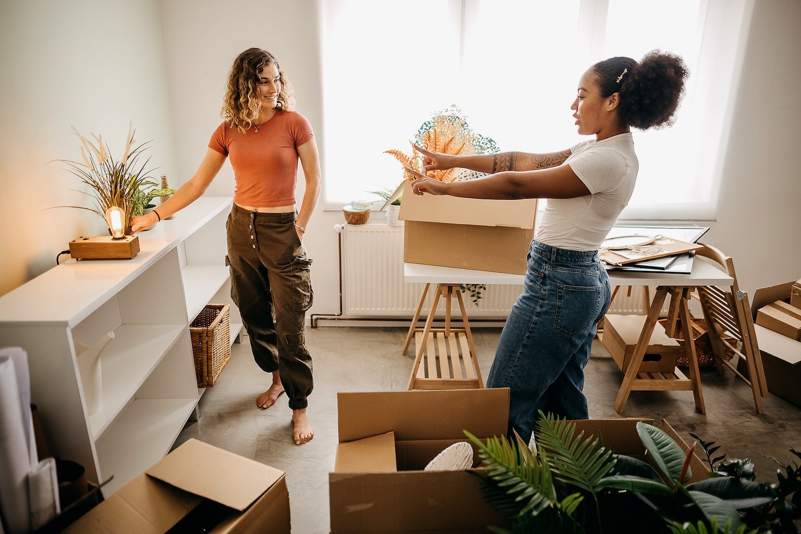 Two friends unpack boxes and arrange things in their new apartment