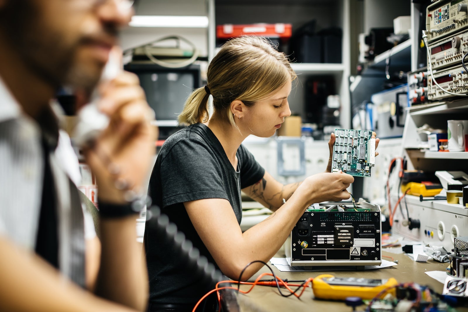 a woman repairs electronics while a man talks on the phone