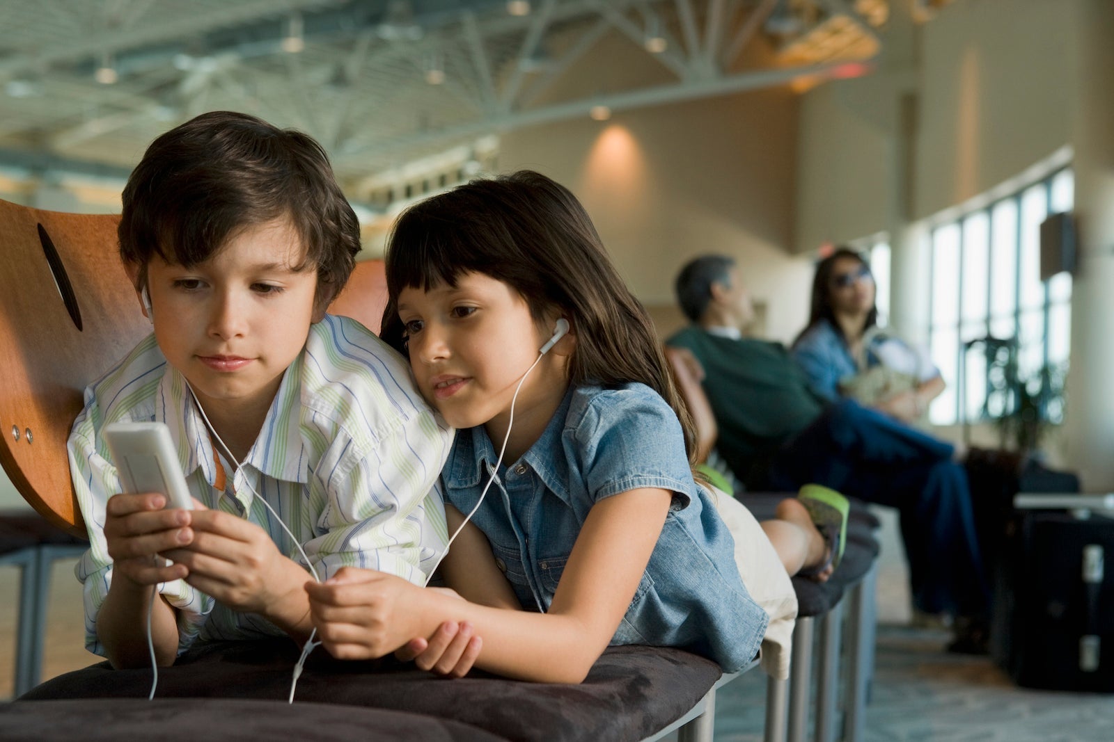 children play a video game while parents linger behind them in an airport lounge