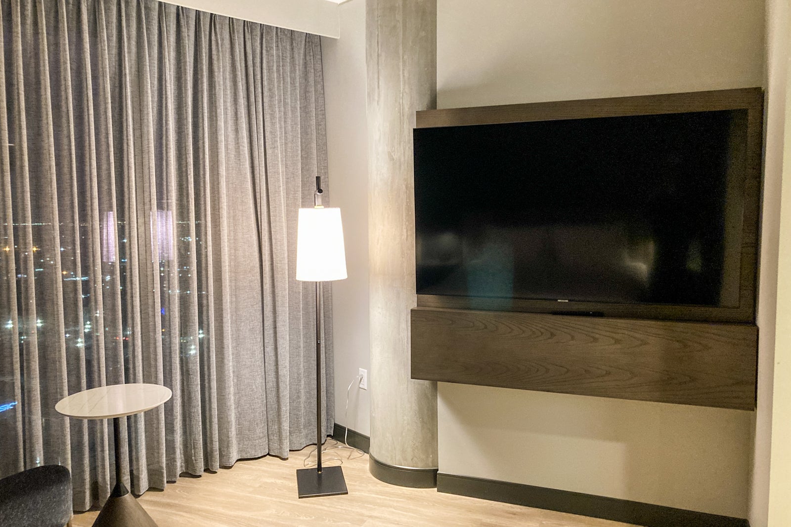 a floor lamp sits between window curtains on the left and a big TV on the right