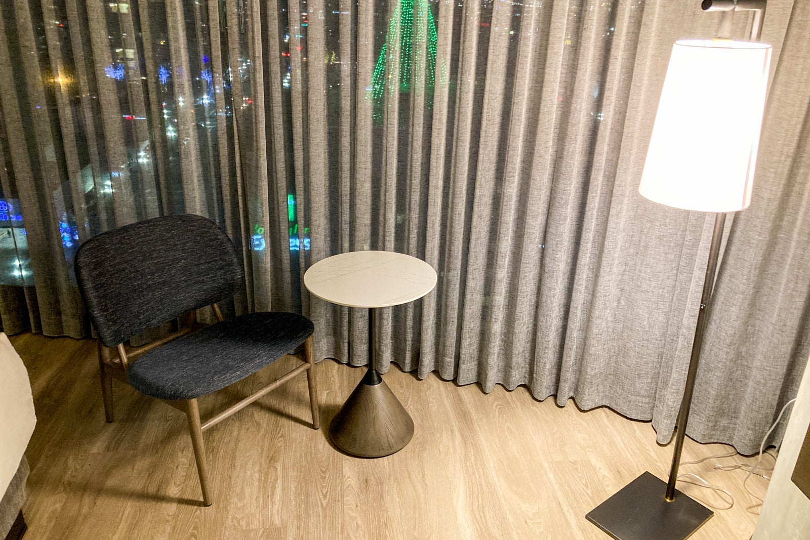 a chair, small table and floor lamp sit near curtains covering floor-to-ceiling windows