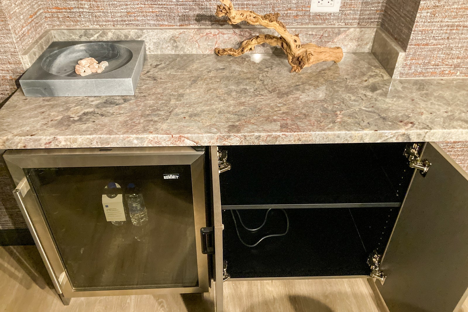 a mini fridge and open cabinet door under a marble countertop