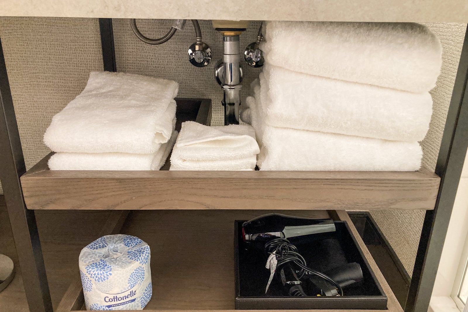 towels and bathroom supplies on shelves under a hotel room sink