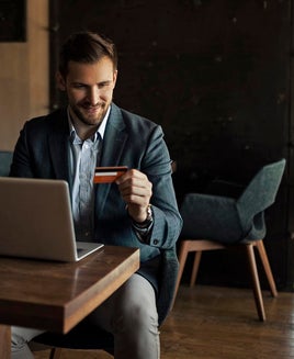 a man in a suit holds a credit card while using a laptop at his desk