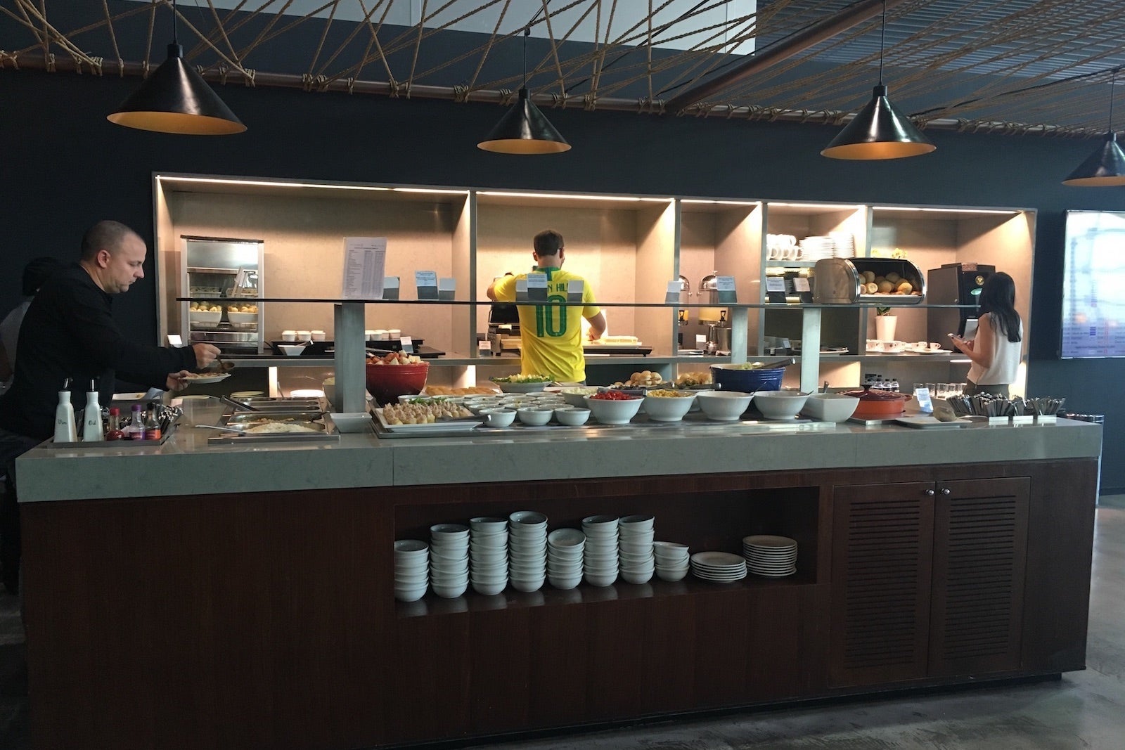 people fill their plates at a food buffet in an airport lounge