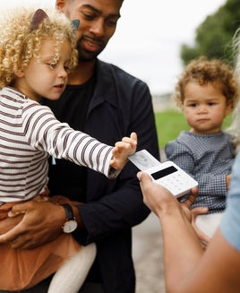 a parent holds a child while the child taps a credit card for payment on a credit card machine