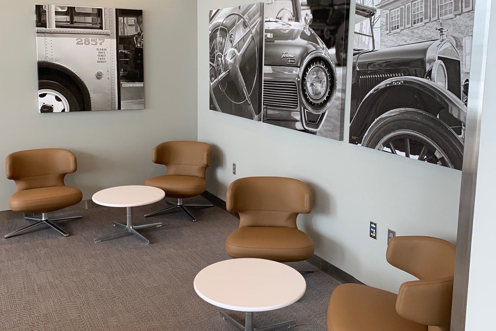 pictures of antique cars on the wall with tables and chairs in an airport lounge