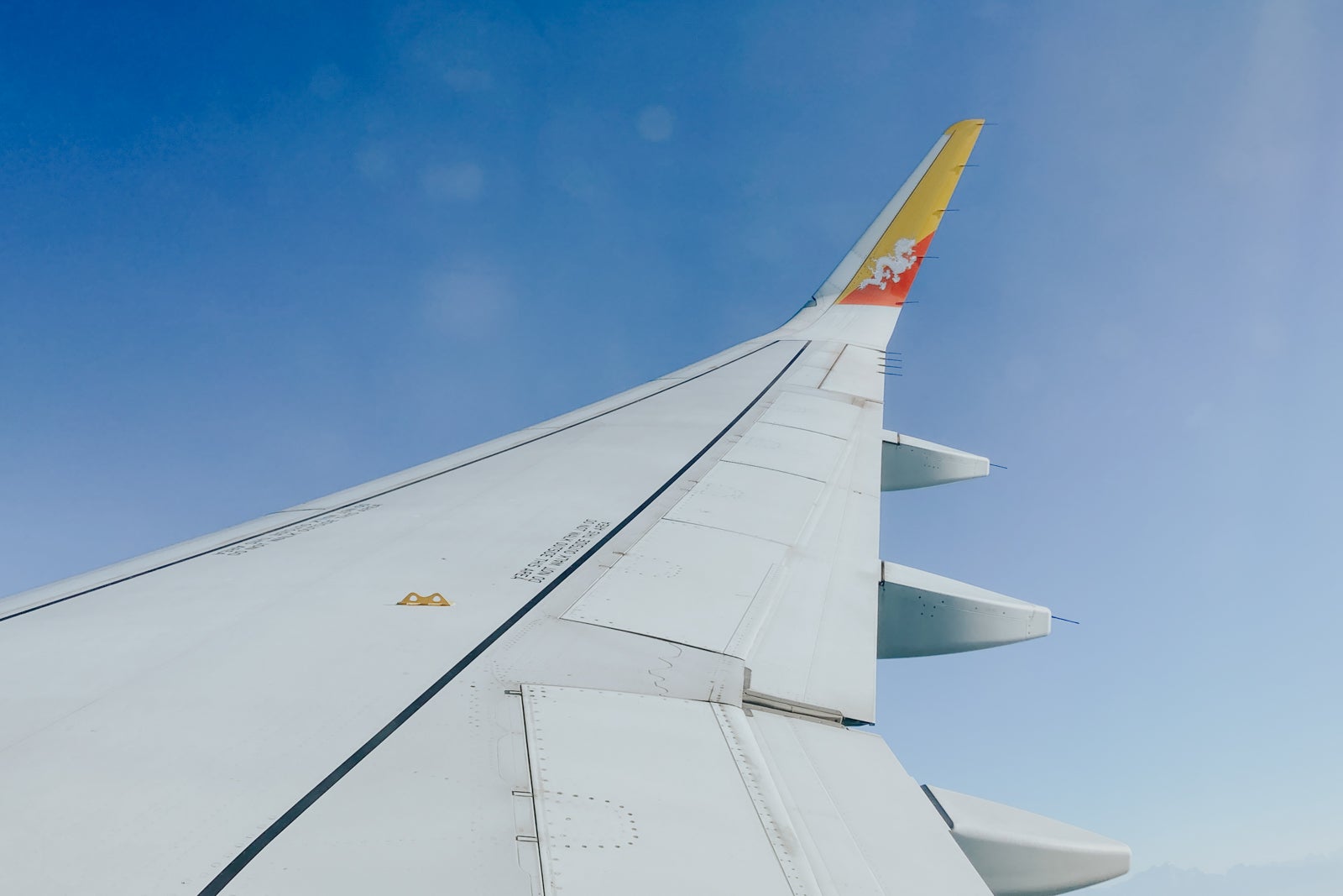looking out an airplane window, the plane's wing is visible with a Bhutanese flag on the wingtip