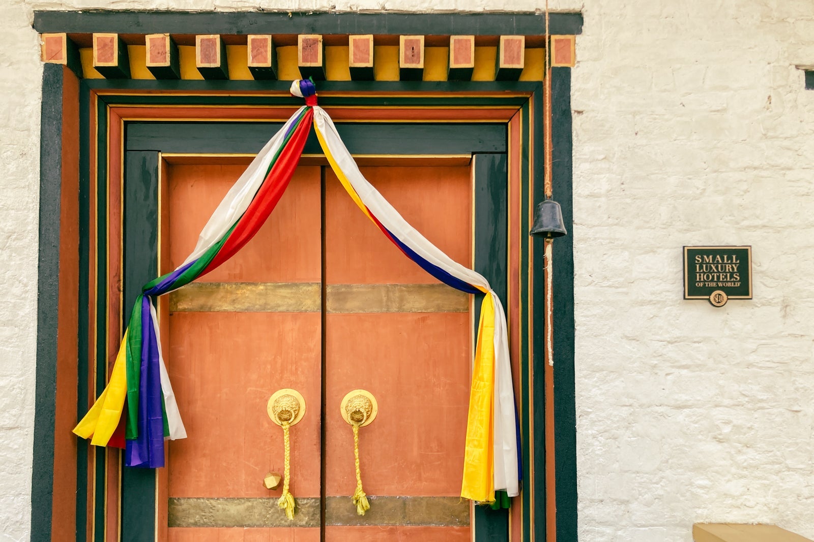 large, double wooden doors adorned with traditional Bhuddist decorations and streamers