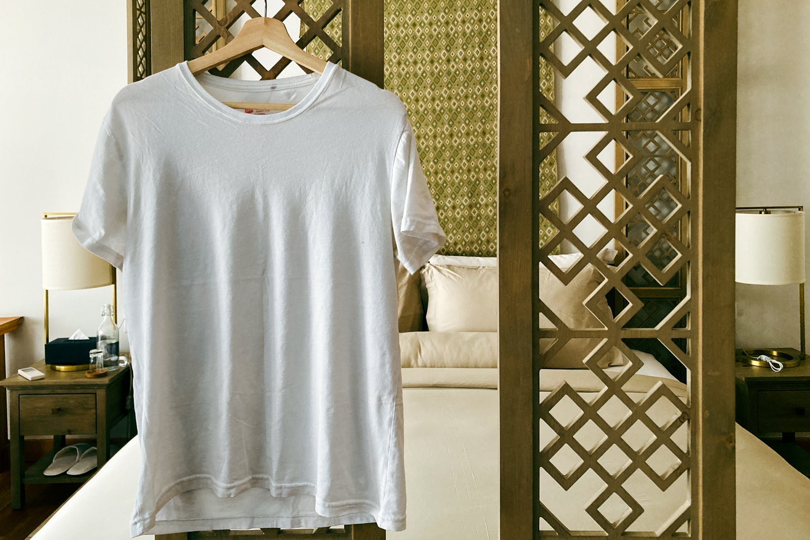 an undershirt hangs on a hanger attached to lattice around a hotel bed