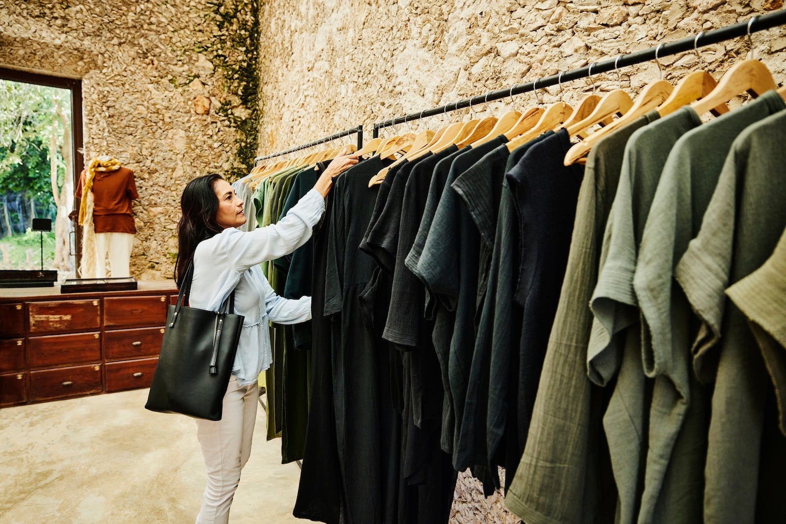 a woman looks at coats on a clothing rack inside a department store