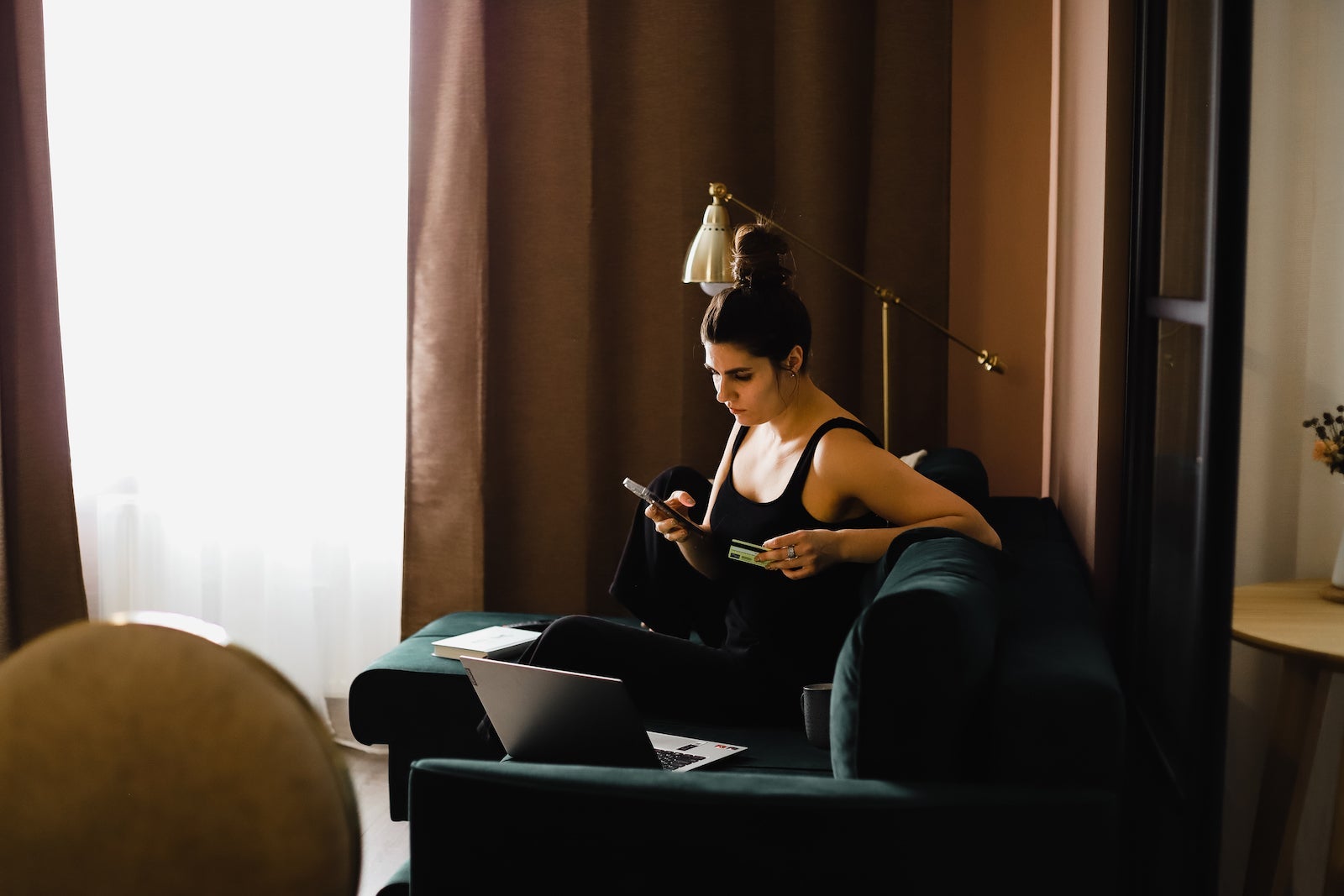 a woman sits on a chair near a window, reading information about her credit card