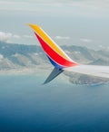 the wing of a Southwest Airlines plane is seen from the plane window, flying over a lake and mountains