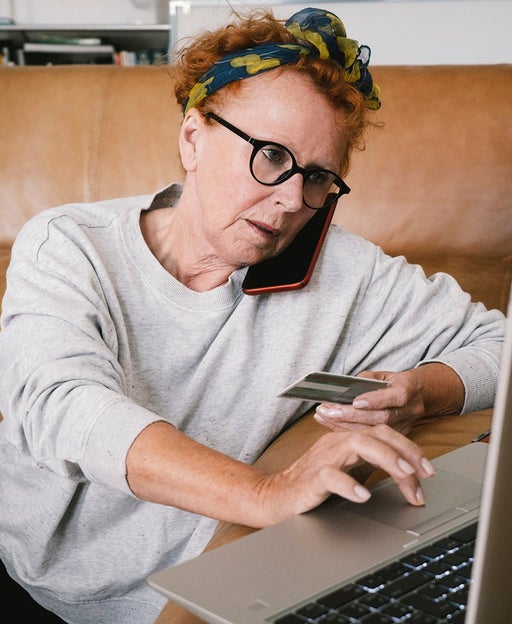 Senior woman talking on smart phone while making online payment through laptop