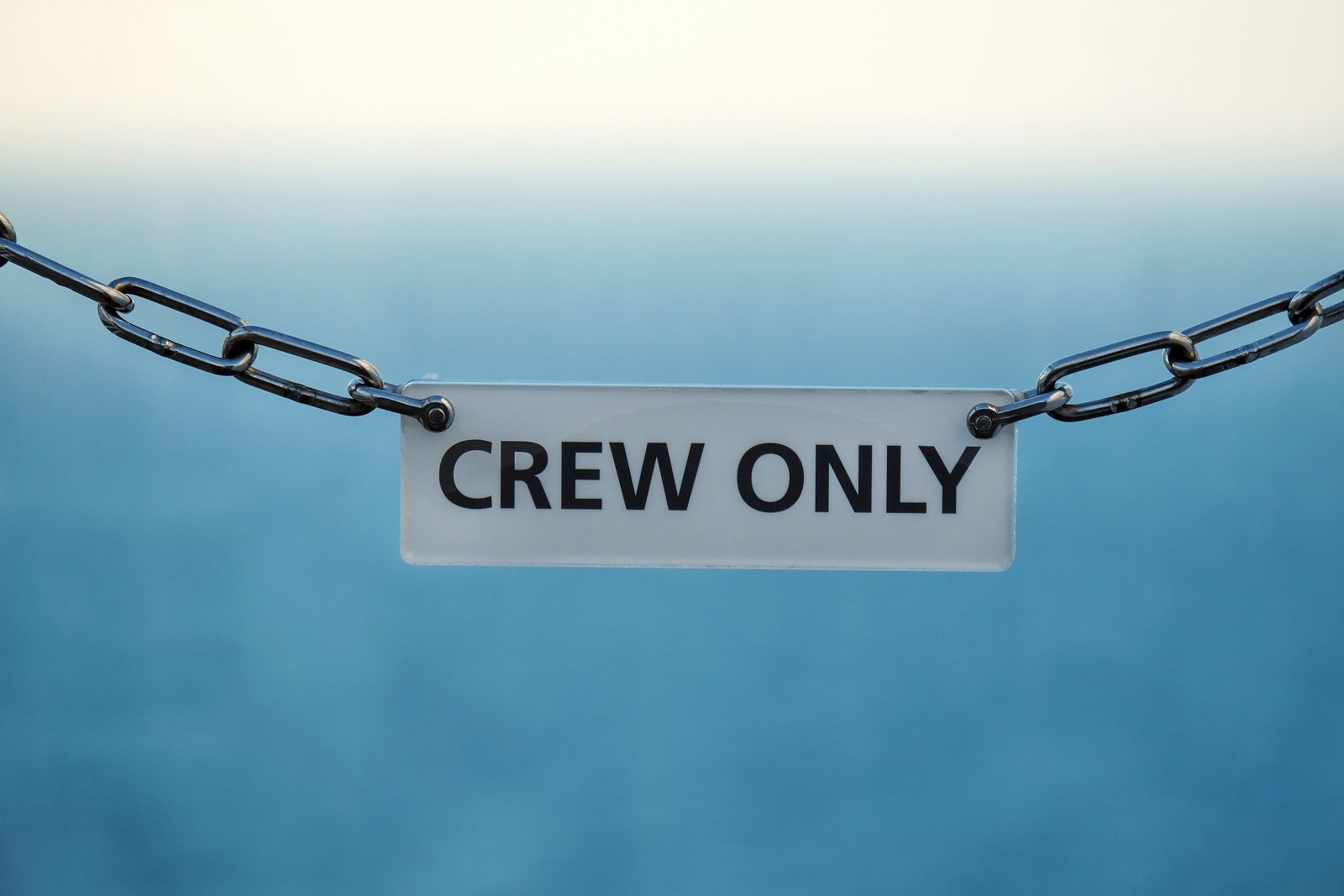 A "crew only" sign hanging from chains with water in the background