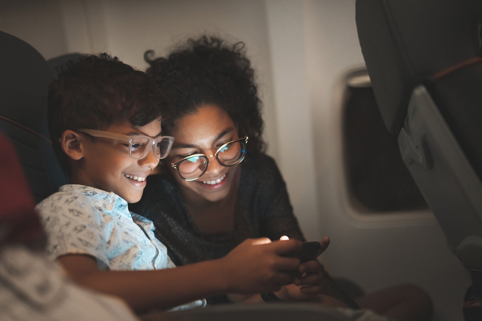2 siblings play a game on a mobile phone while inside an airplane