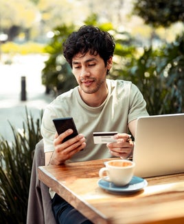 Man using a laptop and smart phone while holding a credit card