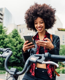 Smiling woman holding credit card while using mobile phone in city