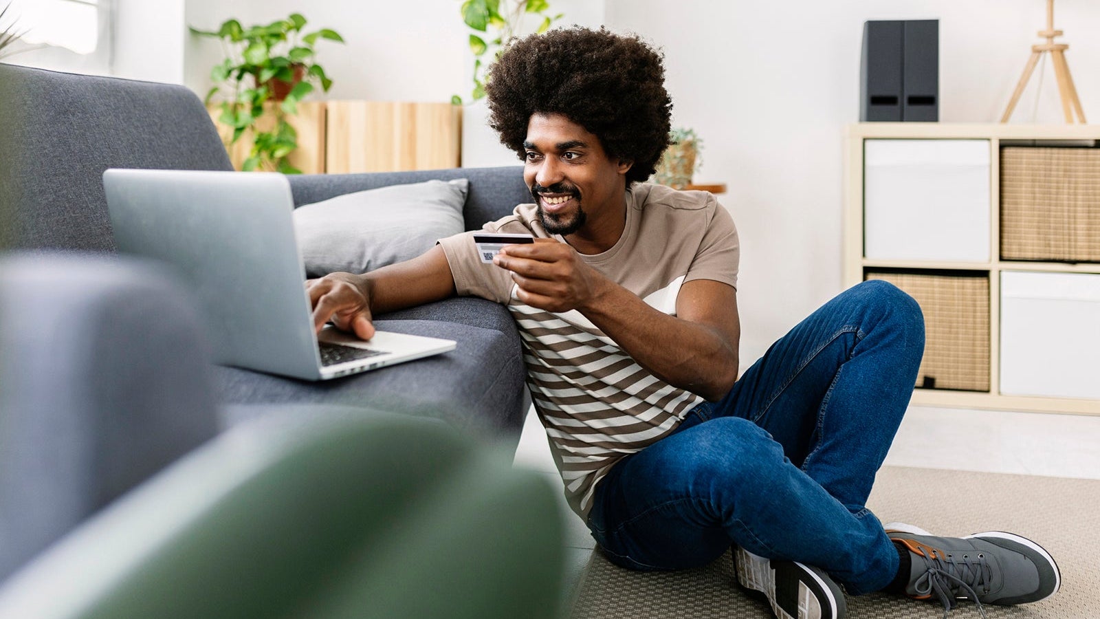 Happy young afro american man holding credit card while shopping online using laptop computer at home