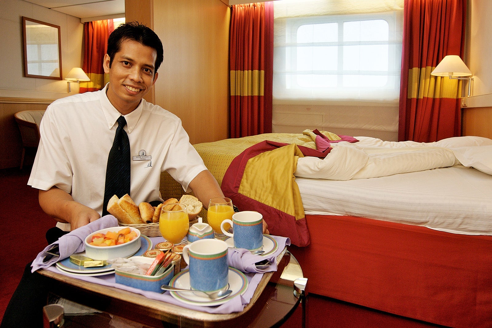 Bell boy serving a breakfast tray in luxury room on cruise ship