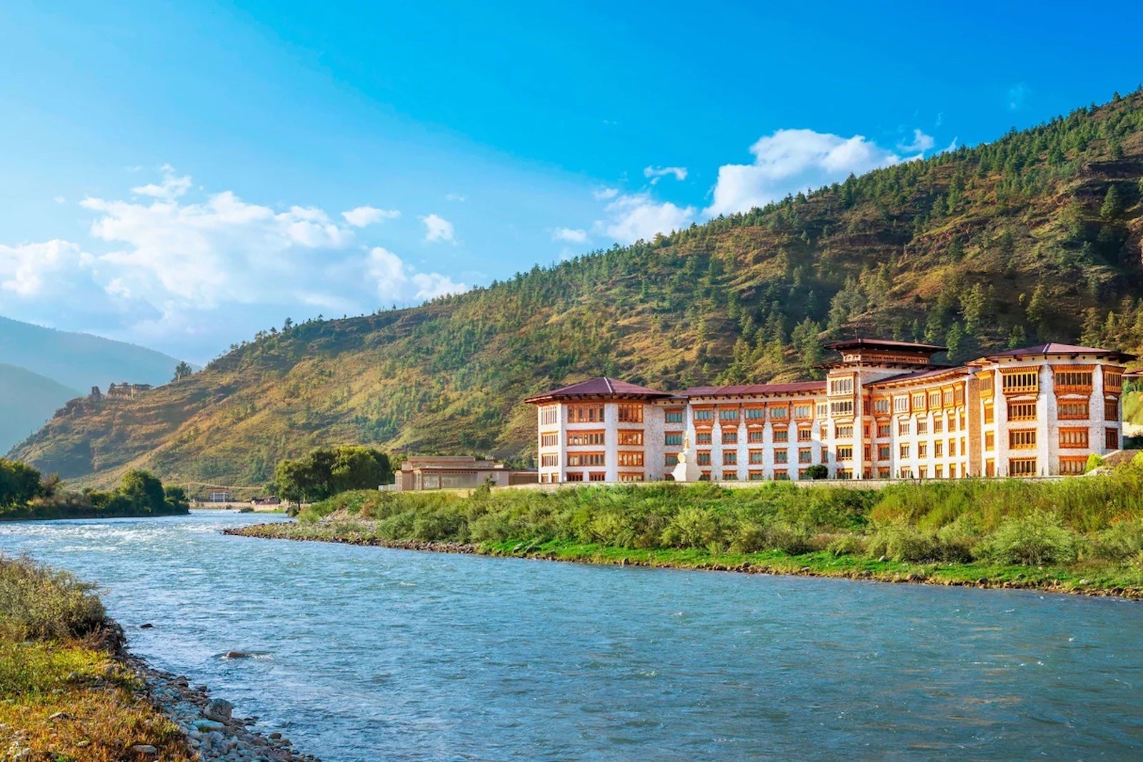 a hotel sits between a river and a mountain