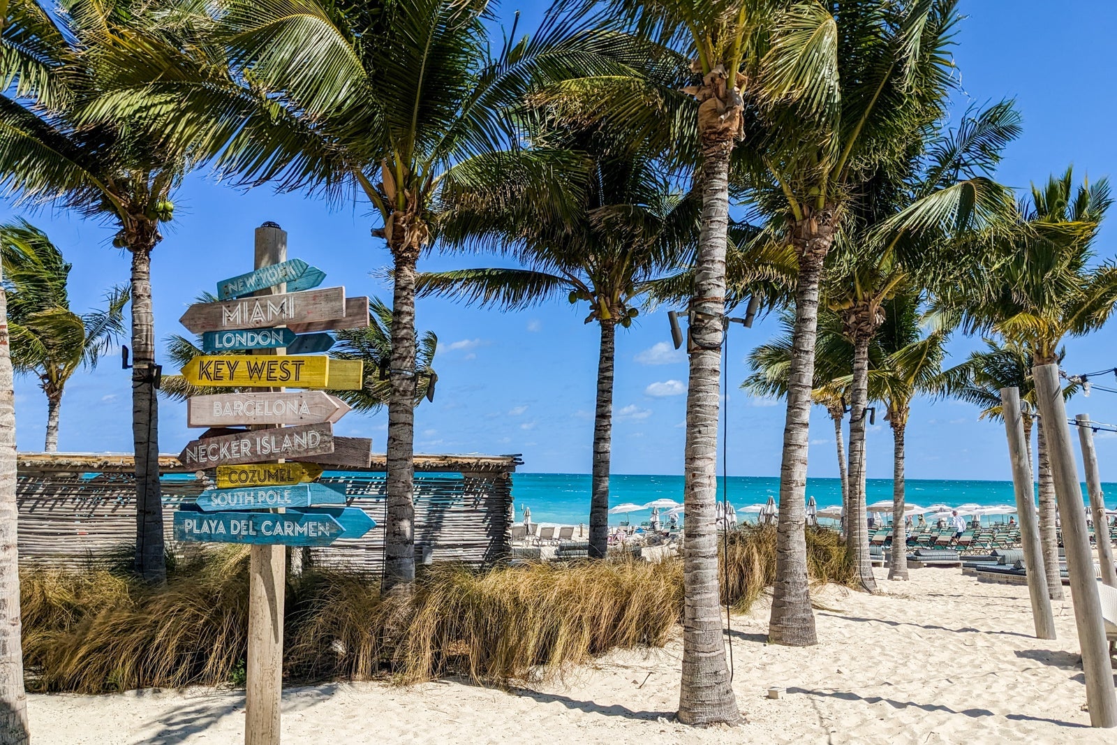 Wooden sign pointing to different places on beach with palm trees