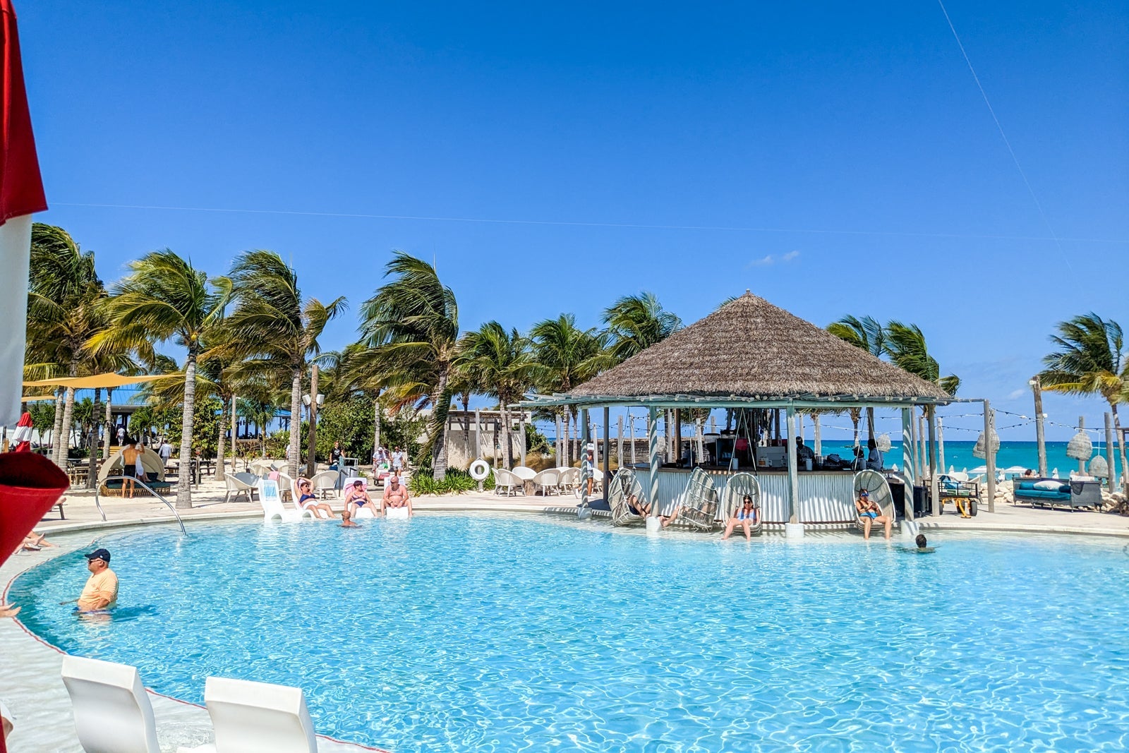 Thatched-roof bar with swing chairs by a pool