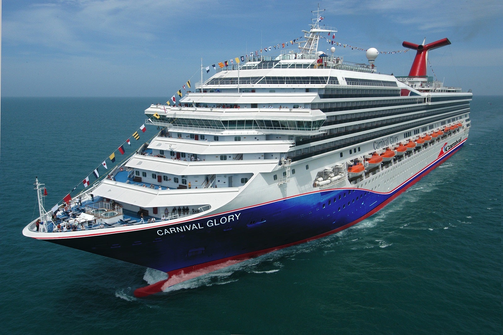 A cruise ship with a blue hull and red funnel sailing on blue-green water