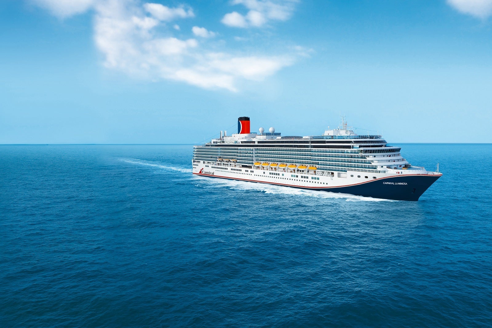A cruise ship with a blue hull and red funnel sailing on blue water with a blue sky and clouds over head