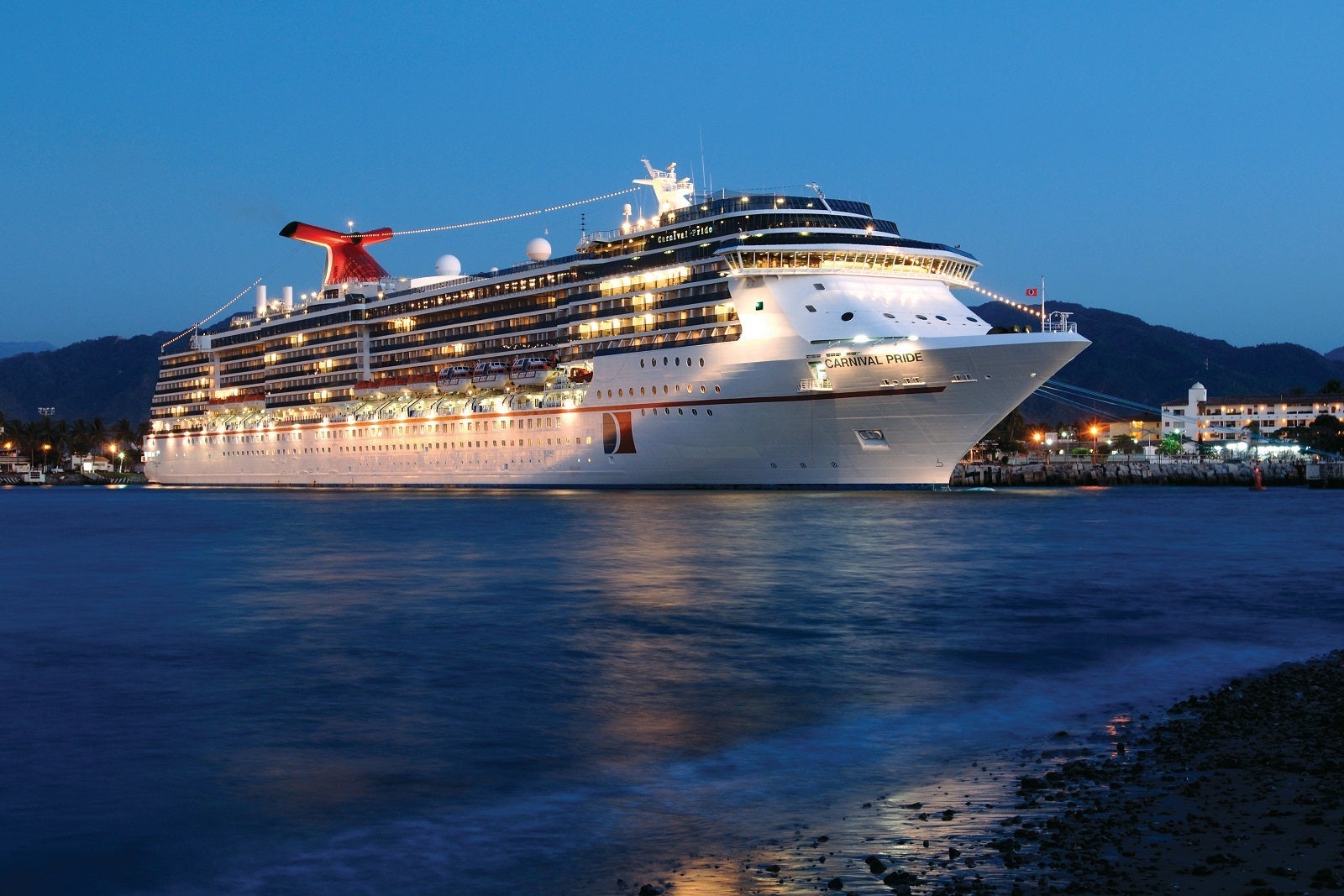 A cruise ship with a red funnel lit up at twilight while docked in port