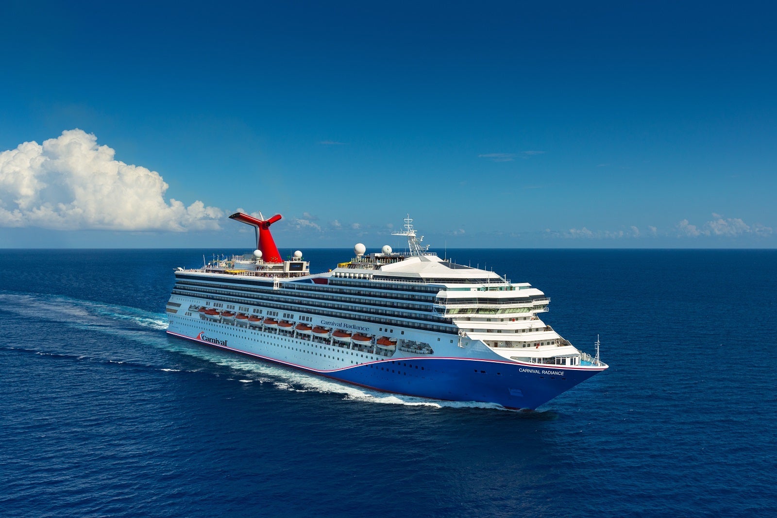A cruise ship with a blue hull and a red funnel sailing on blue water with blue sky and a cloud over head