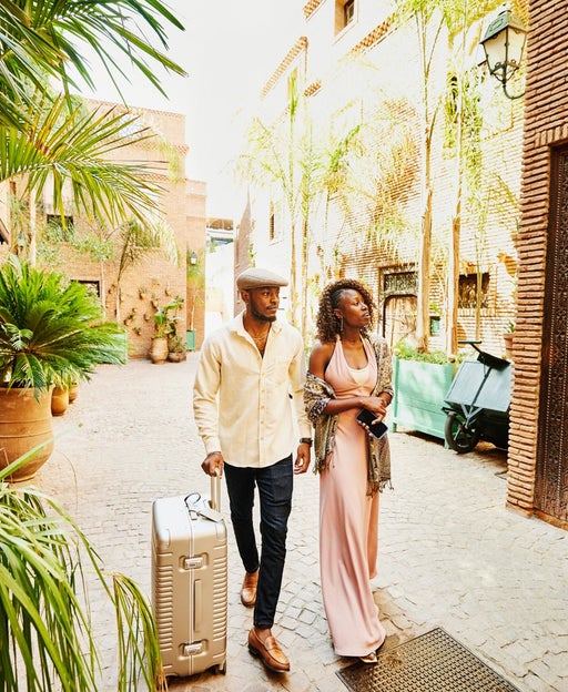 Wide shot of couple arriving in hotel courtyard with rolling luggage