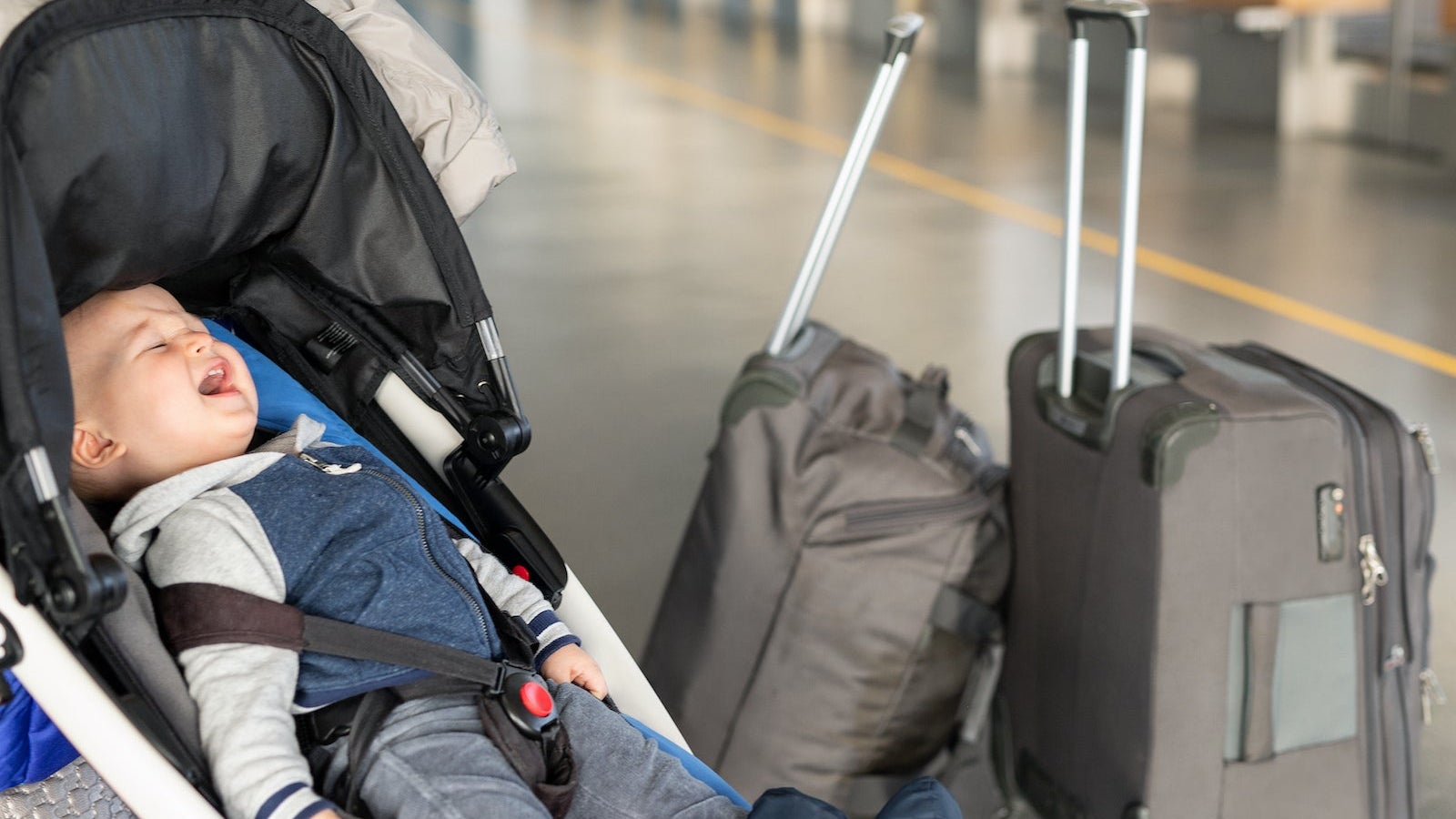 Screaming baby boy sitting in stroller near luggage at airport terminal. Child in carriage near check-in desk counter. Children tears , panic and hysterics. Travelling with small children concept