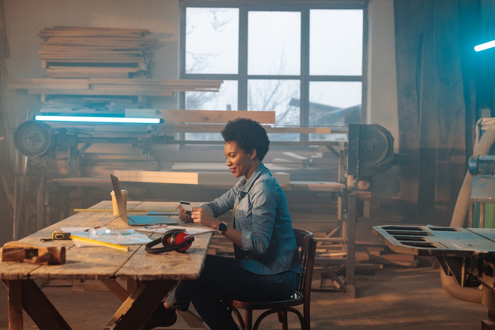 A female African American carpenter is in her workshop ordering material online on her laptop and paying with her credit card.