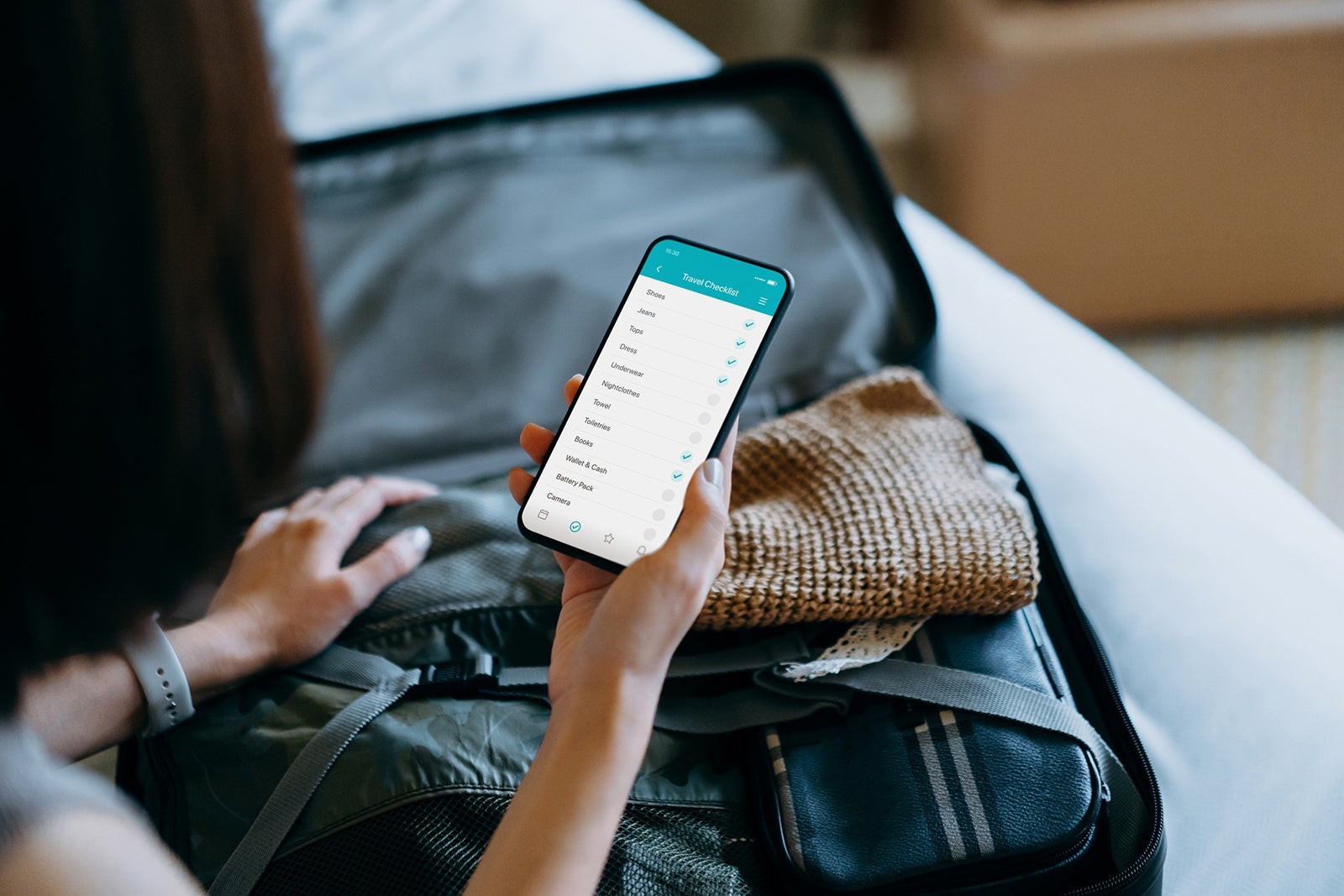 Woman looking at packing list on phone in front of suitcase