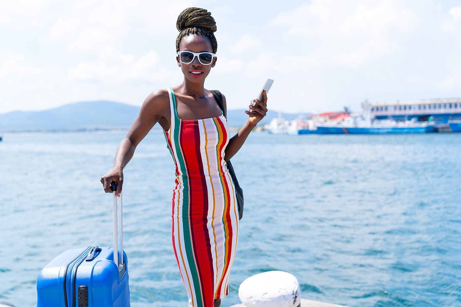 African woman with suitcase walking on harbor and talking on smart phone